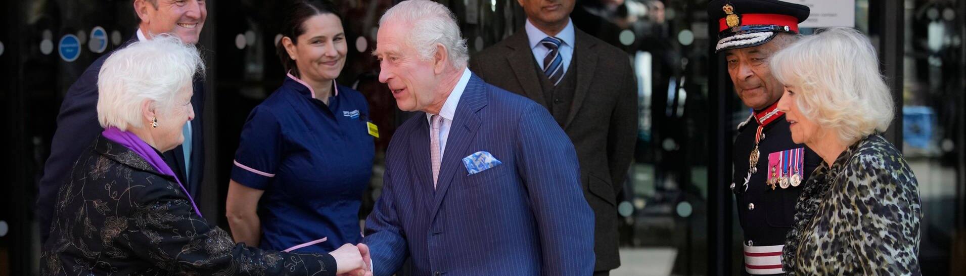 König Charles III.(M) und Königin Camilla (r) von Großbritannien werden bei ihrem Besuch im Macmillan Cancer Centre des University College Hospital begrüßt. 